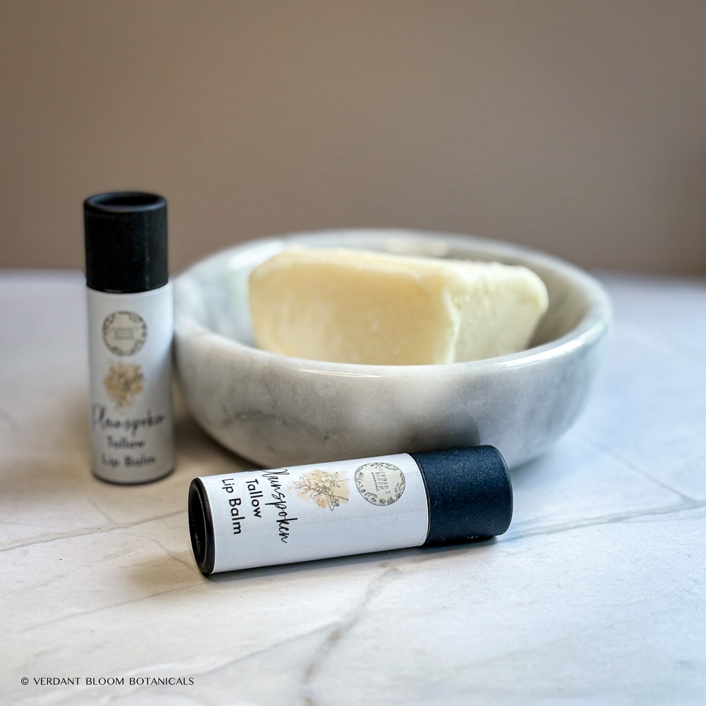 Two tubes of Plainspoken lip balm next to bowl holding shea butter